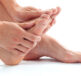 Why do we get fungal nail infections? A person with bare feet is holding on to their foot with both hands