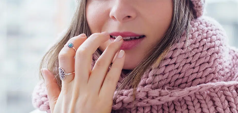 A woman wearing a pink scarf applying Dermal Therapy Lip Balm to her dry chapped lips in Winter