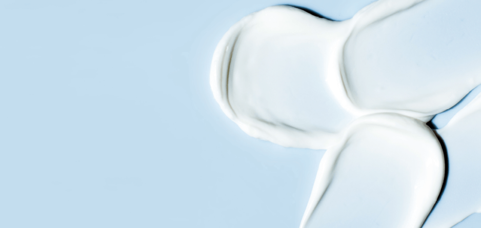 A moisturiser with urea in it is spread across a blue surface, forming four distinct white cream blobs.