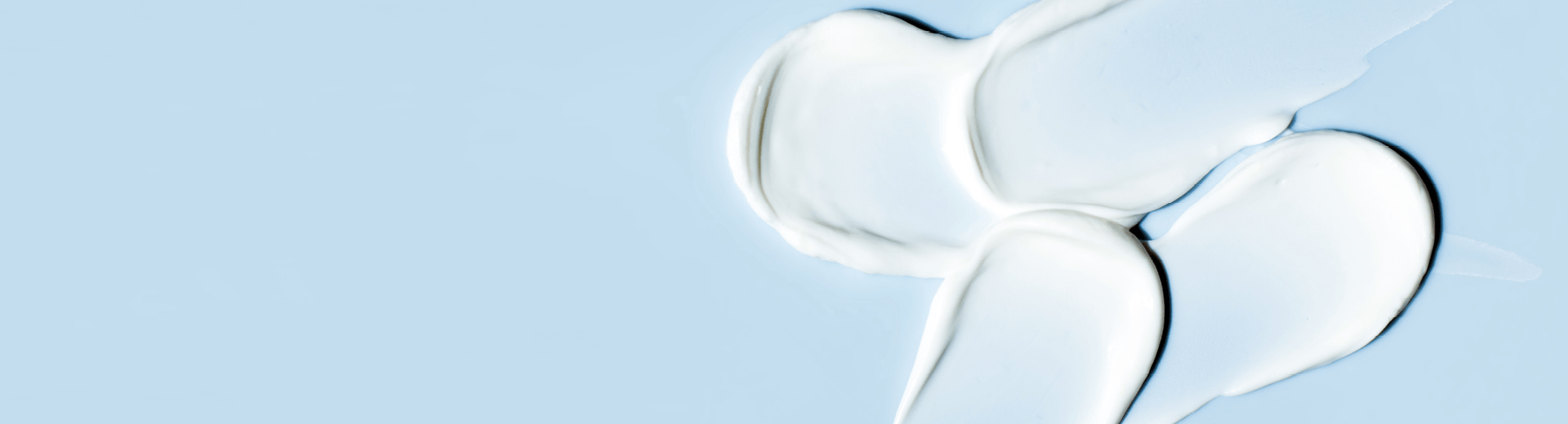 A moisturiser with urea in it is spread across a blue surface, forming four distinct white cream blobs.