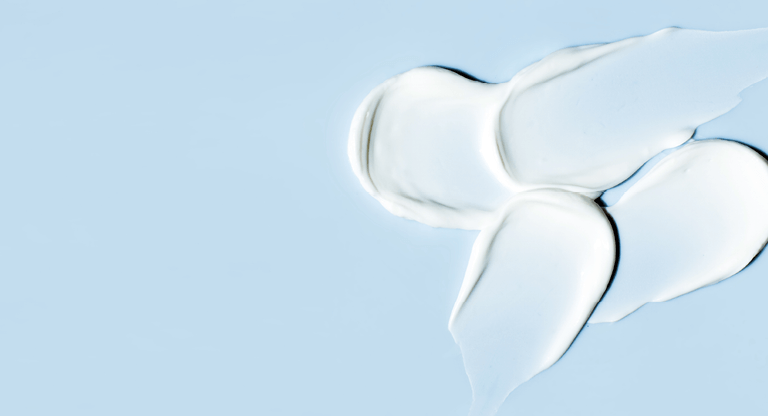 A moisturiser with urea in it is spread across a blue surface, forming four distinct white cream blobs.