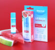 Dermal Therapy Lip Balm Watermelon packaging and lip balm shown with sliced watermelon on a red background