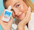 Image of a smiling model holding her face on one hand while the other is holding the Dermal Therapy Sebum Control Serum packaging
