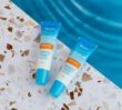 Two Dermal Therapy Lip Balm SPF50+ tubes on a terrazzo surface beside blue water.
